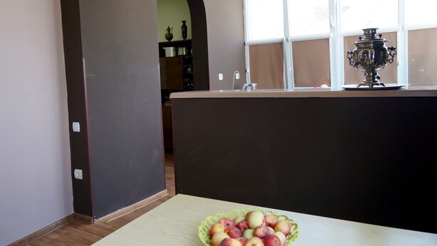 A kitchen with a fruit bowl on the counter, a window with a decorative item, and a door leading to another room. - Mimino (Kutaisi)