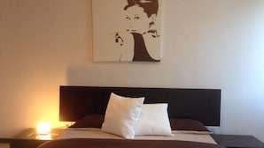 Habitación de hotel con cama, dos almohadas, mesita de noche con lámpara y una obra de arte colgada en la pared.