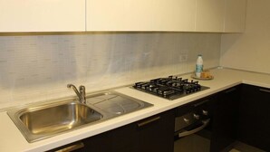 Una cocina moderna con un lavamanos de acero inoxidable, una estufa a gas y una encimera blanca.