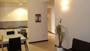 Una cocina moderna con armarios blancos, una mesa de comedor con sillas, una planta en maceta y un sofá en la sala de estar.