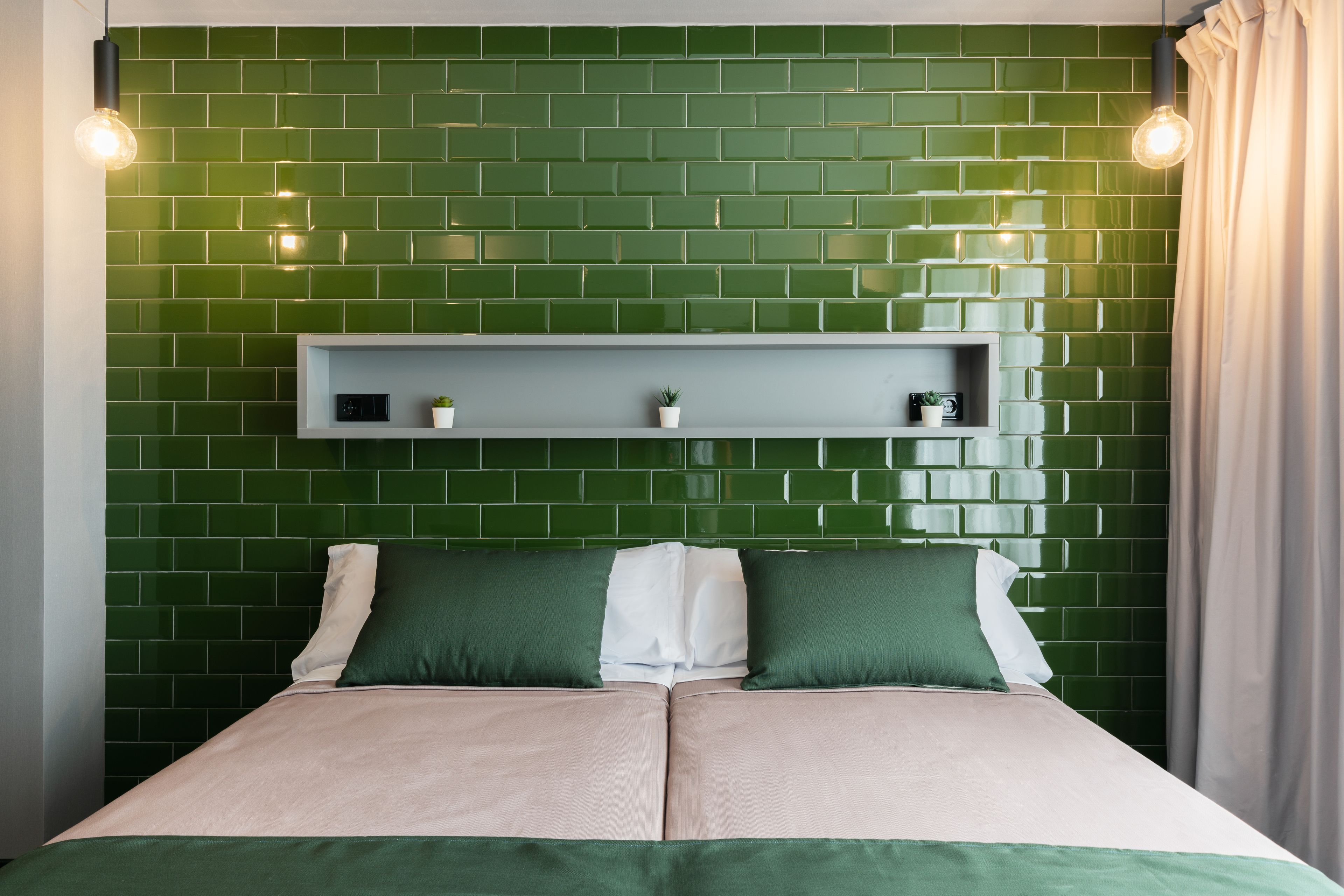 A bed with two pillows, a headboard with a shelf, and green tiled walls.