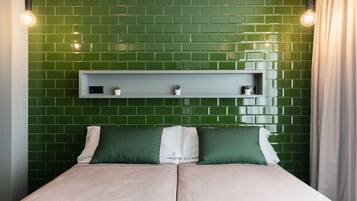 A bed with two pillows, a headboard with a shelf, and green tiled walls.