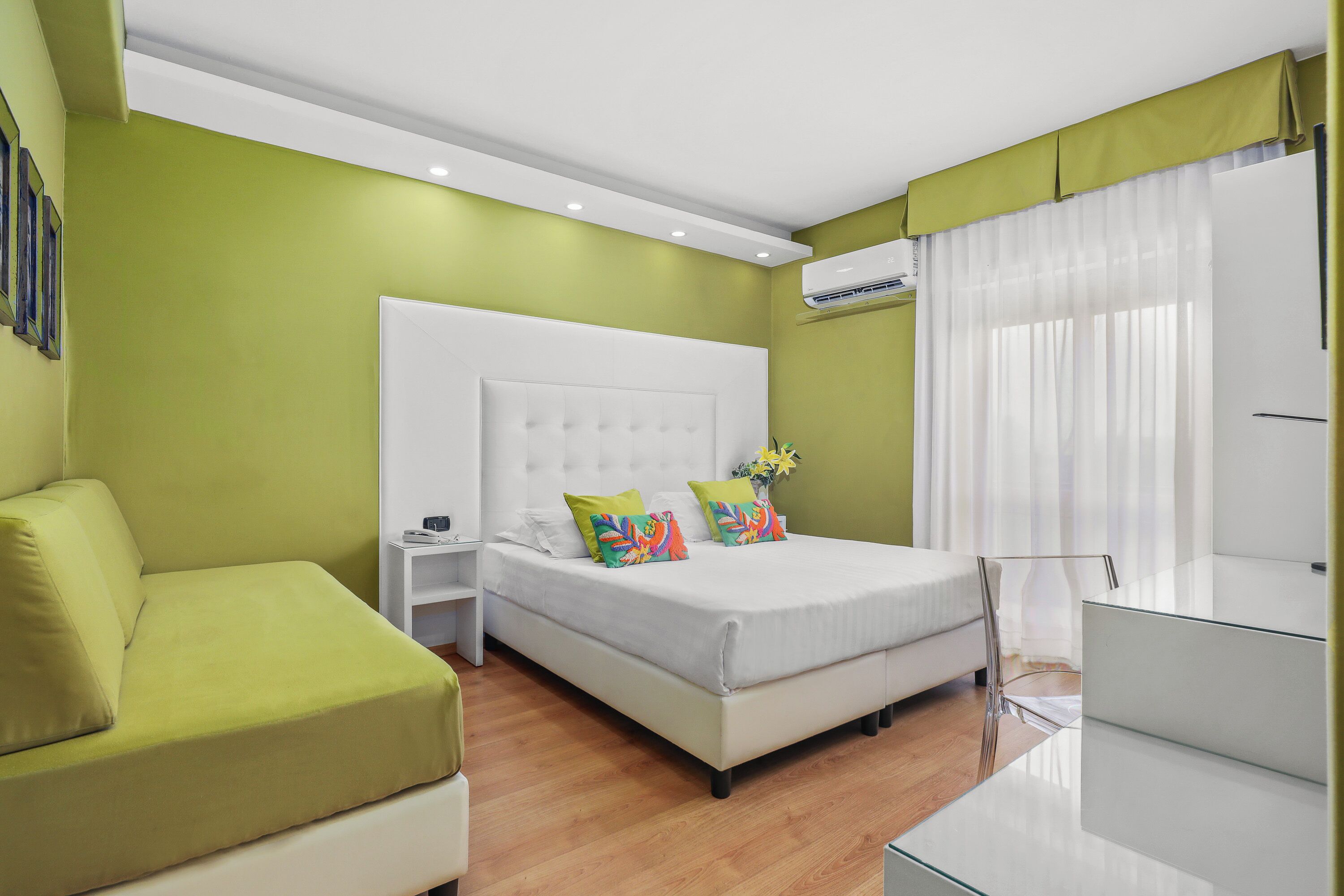 Une chambre moderne avec un grand lit, un canapé vert, une table en verre et une table de chevet blanche.