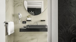 Un baño con pared de mármol, un espejo redondo, un lavabo negro, un secador de pelo y un perchero para toallas.