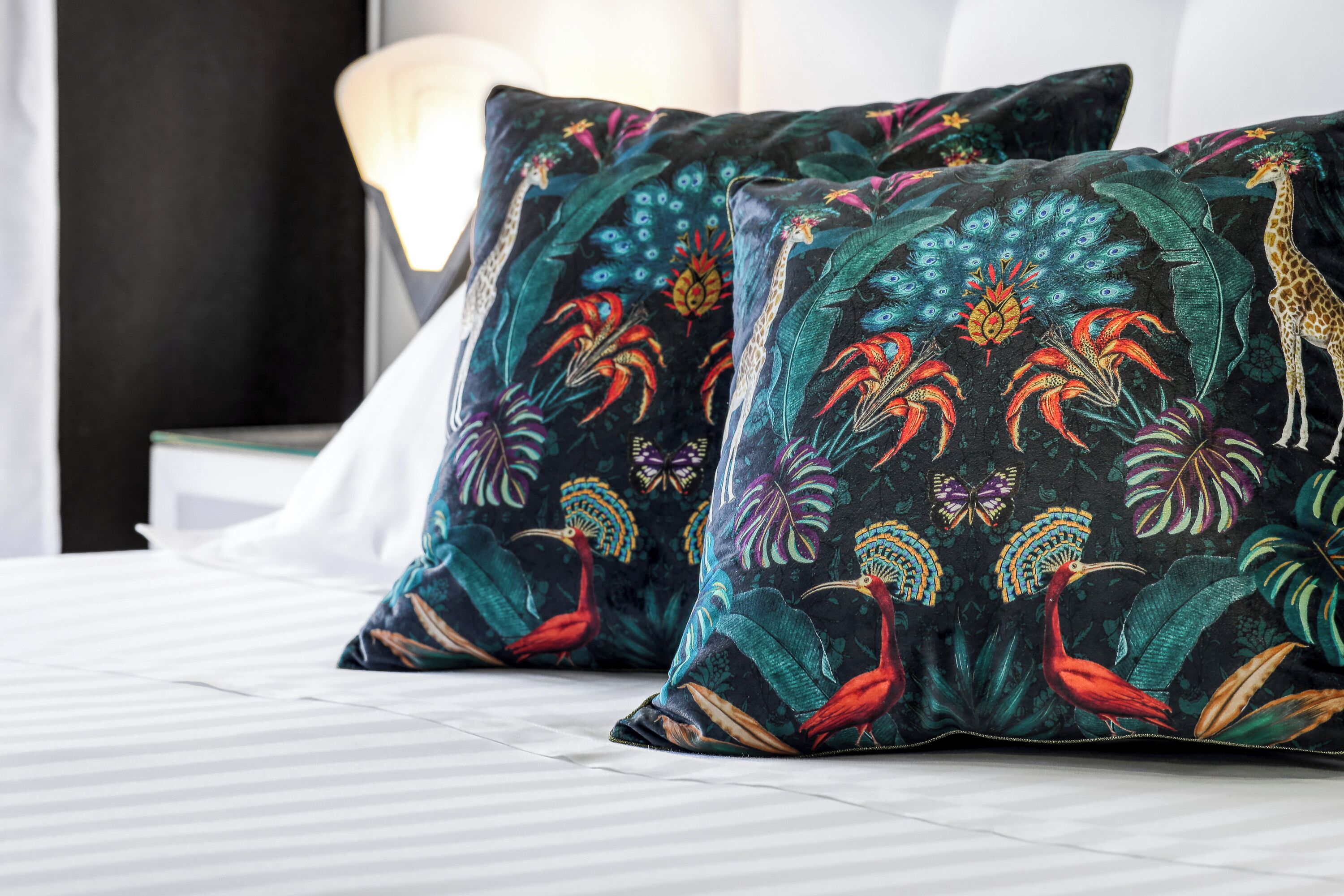 Een bed met twee sierlijke kussens met afbeeldingen van tropische vogels en bladeren.