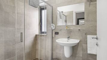 Un baño moderno con cabina de ducha de vidrio, un lavamanos pedestal blanco y un espejo grande.