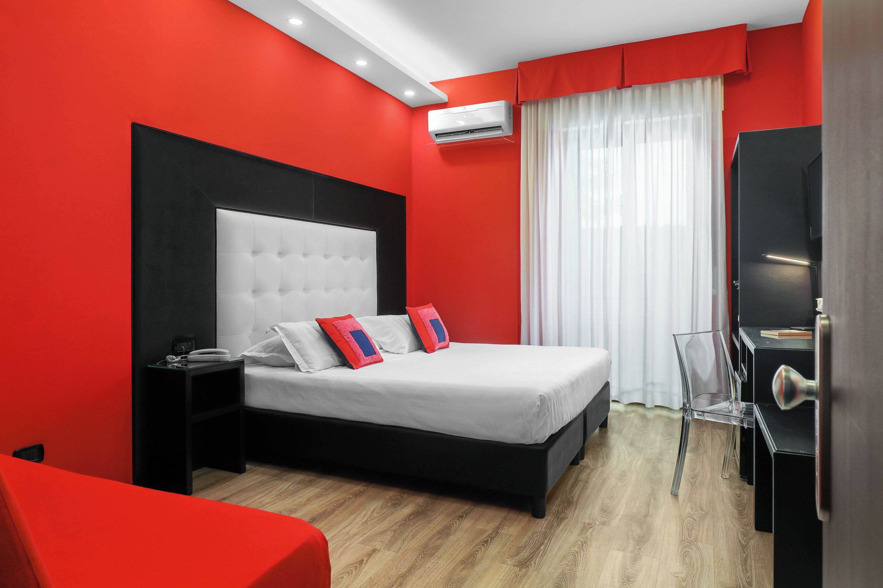 Ein modernes Hotelzimmer mit einem großen Bett, einem Nachttisch, einem Sessel und einem Schreibtisch mit einem Computer.