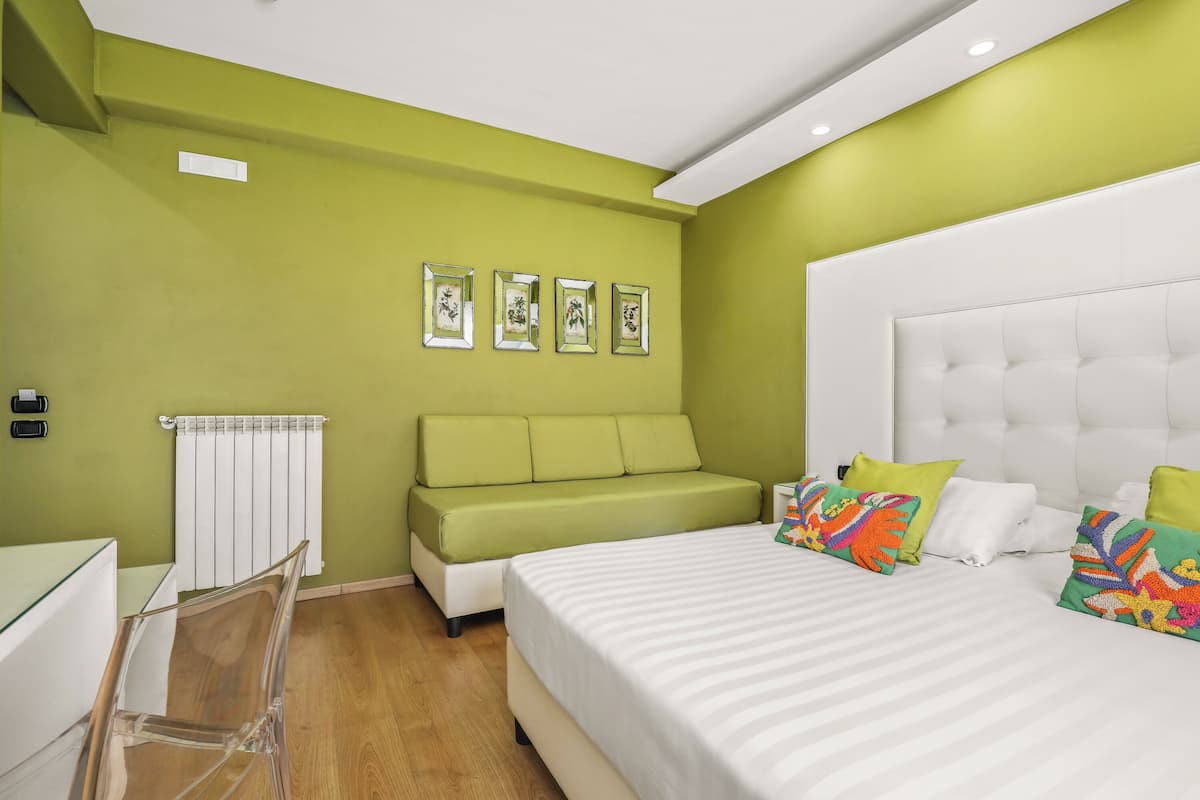 A bedroom with a green wall, a white bed, a green sofa, and a white radiator.