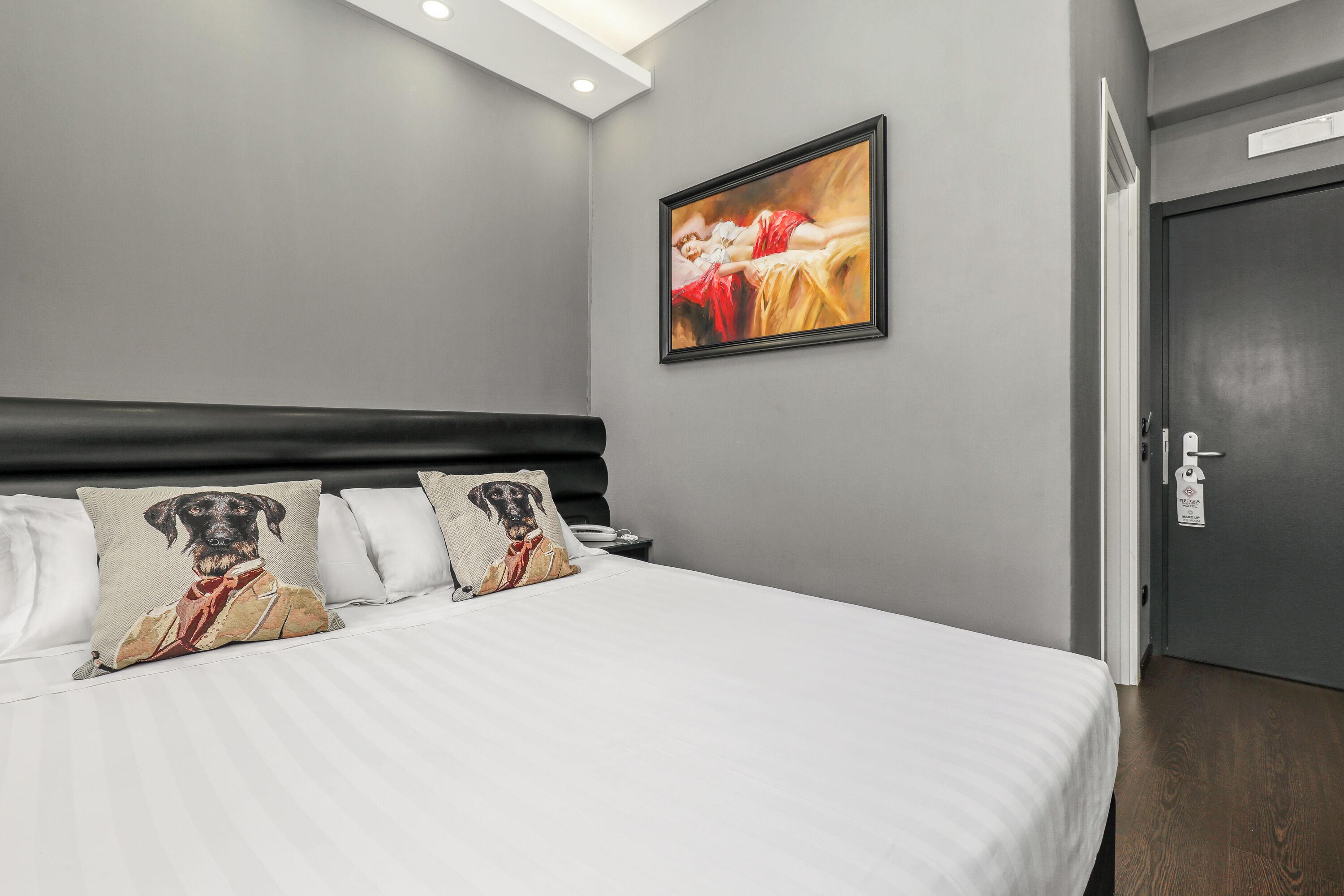 Ein Hotelzimmer mit einem großen Bett, einem Kopfteil, einem Bild an der Wand und einer Tür.