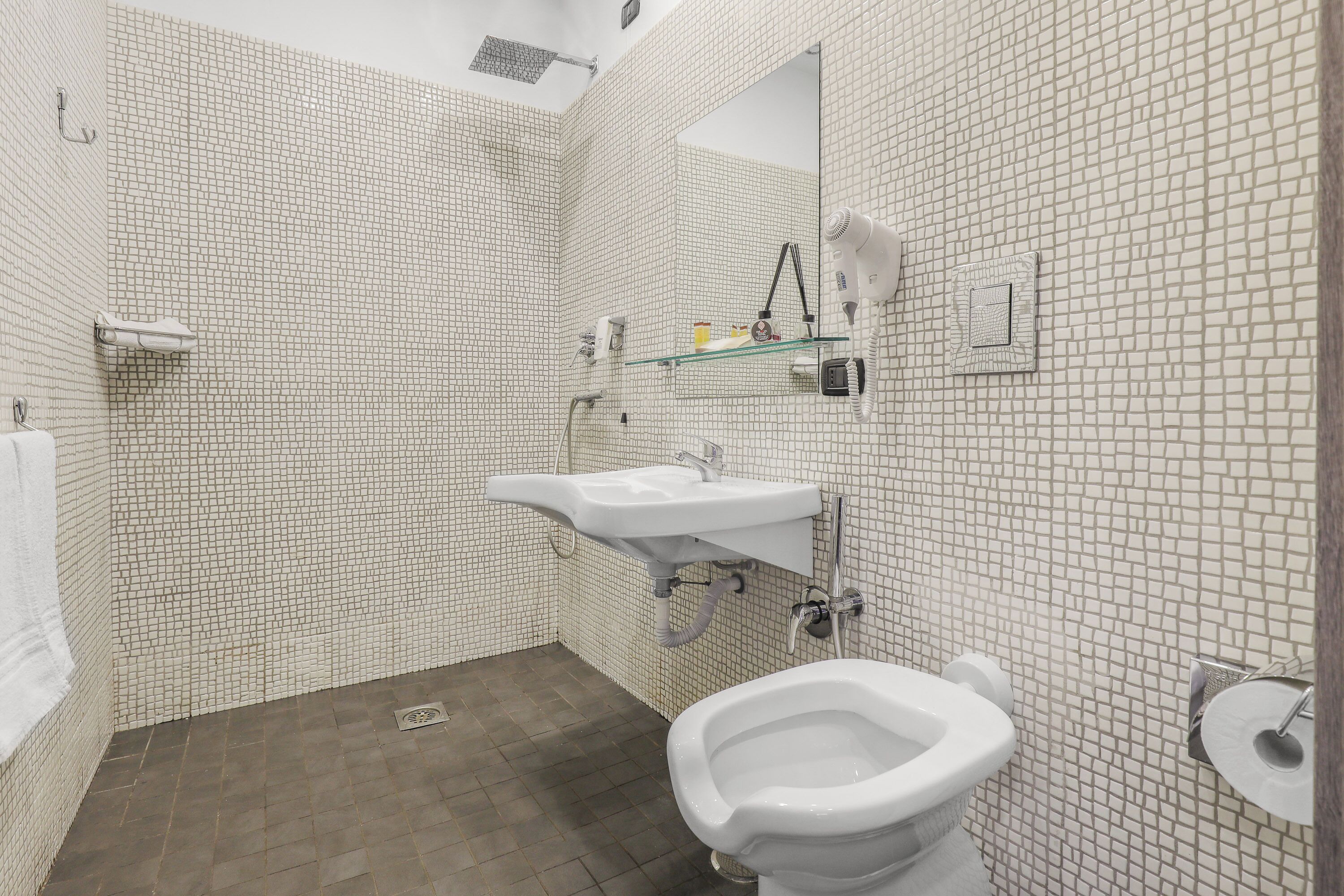 A bathroom with a white tiled floor, a white sink, a bidet, and a mirror.