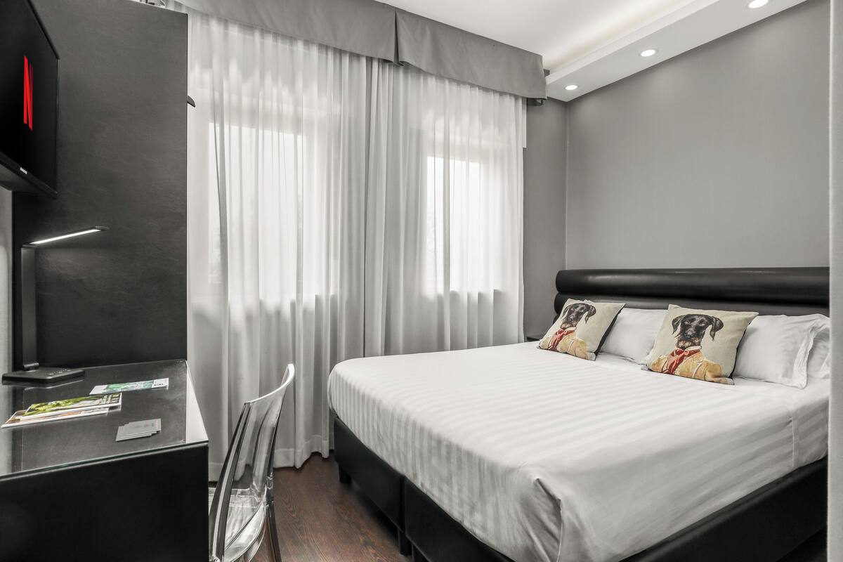 A modern hotel room with a large bed, a desk, and a chair.