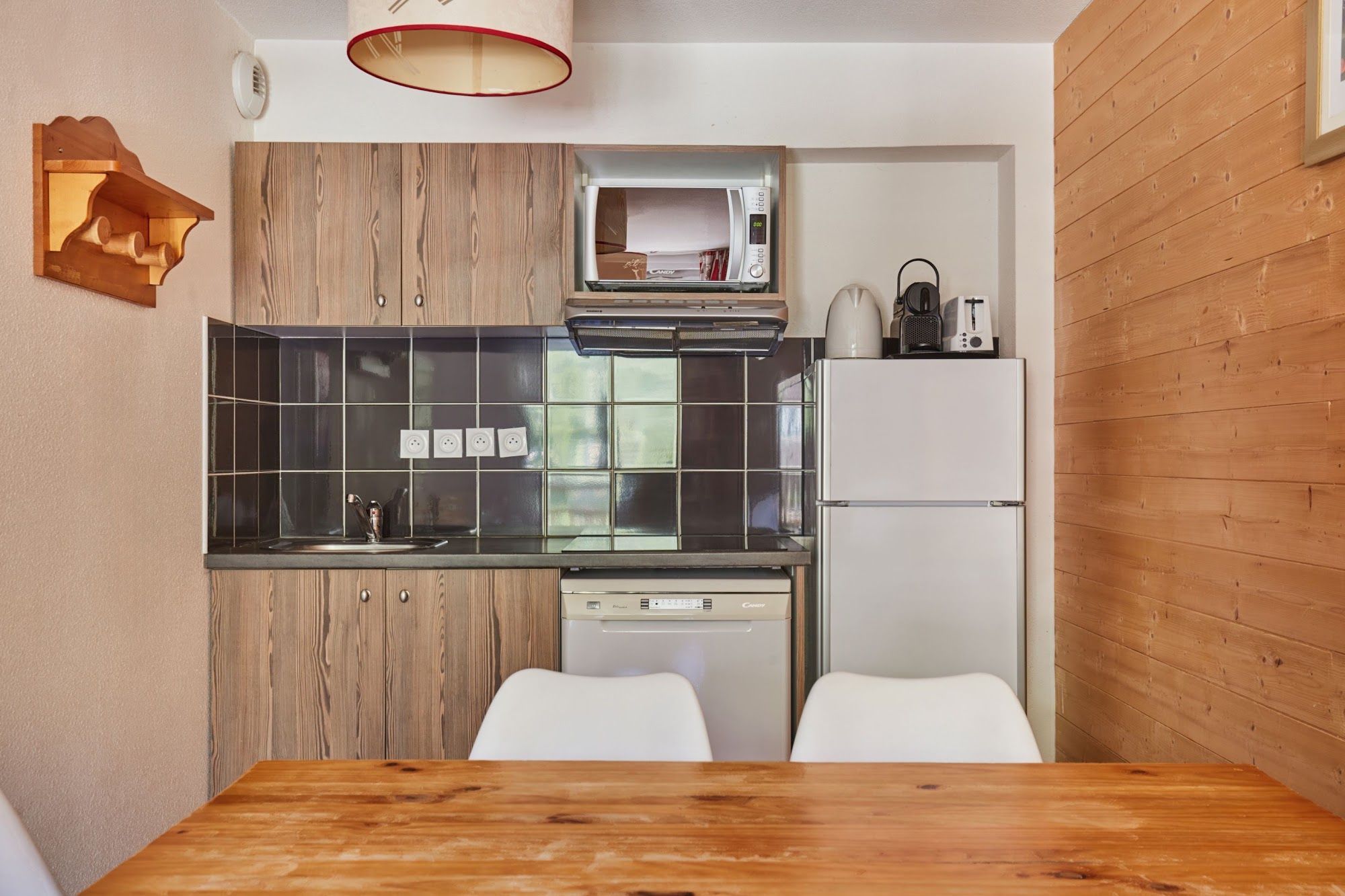 Cocina compacta con microondas, tostadora y refrigerador, armarios de madera y un comedor con mesa y sillas de madera.