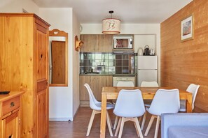 A compact kitchen with a dining area, wooden cabinets, and a modern pendant light.