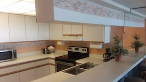 A modern kitchen with white cabinets, a microwave, a stove, and a sink. There are two potted plants on the counter. - Right On the Beach !  Vacation Condo ! (Panama City Beach)