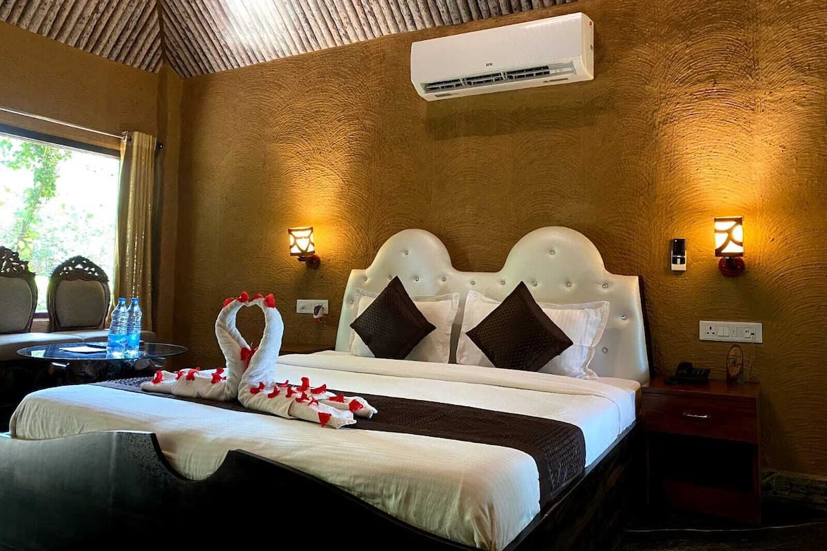 Habitación de hotel con una cama, dos lámparas fijadas a la pared, un aire acondicionado y una mesita con una botella de agua.