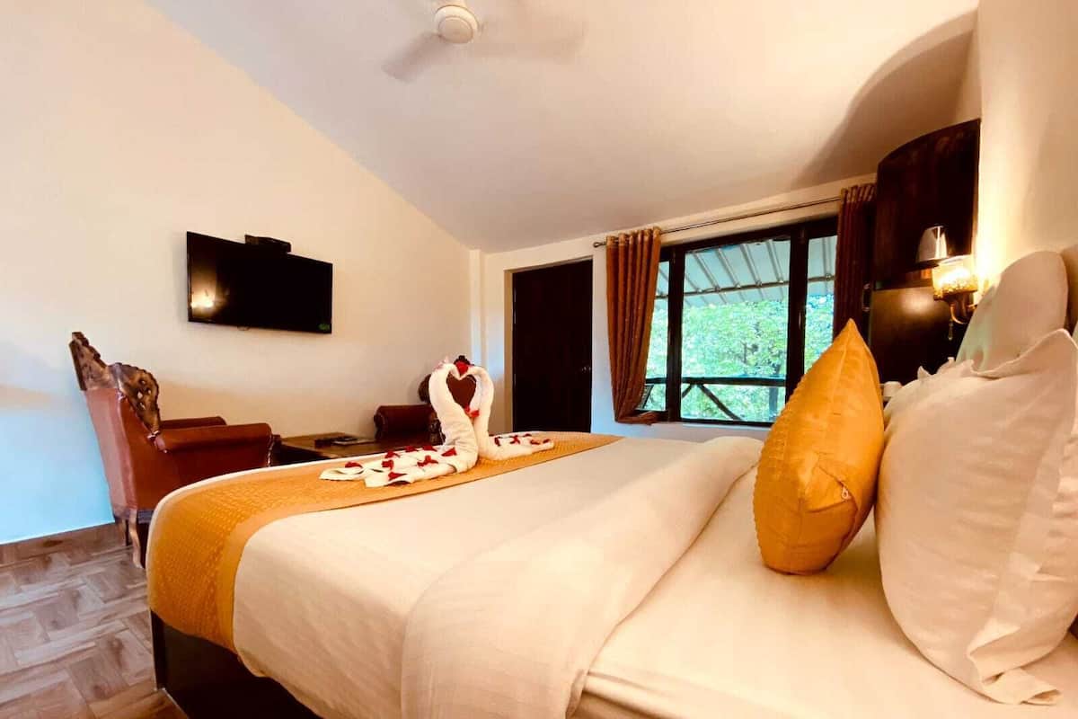 Habitación de hotel con cama, televisor de pantalla plana, ventana con cortinas y suelo de madera.