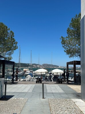 A marina with boats docked, outdoor seating, and a clear view of the water and distant hills.