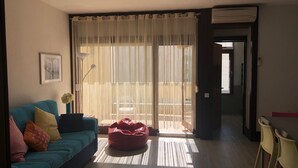 Un salon comprenant un canapé, un fauteuil en forme de poire rouge, une lampe sur pied et un coin repas avec des chaises.