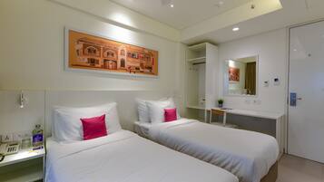 A hotel room with two beds, a desk with a phone and a bottle, a mirror, and a painting on the wall.