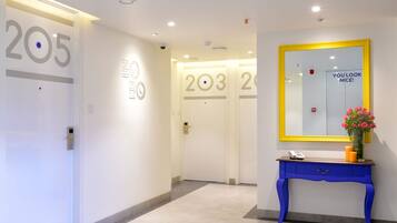 A hotel hallway with doors numbered 205 and 203, a blue console table with a phone and candles, and a mirror with a yellow frame.