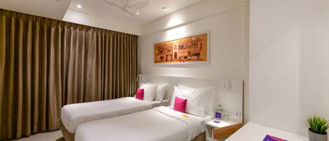 Quarto de hotel com duas camas, um ventilador de teto, um quadro, uma mesa de cabeceira e uma planta.