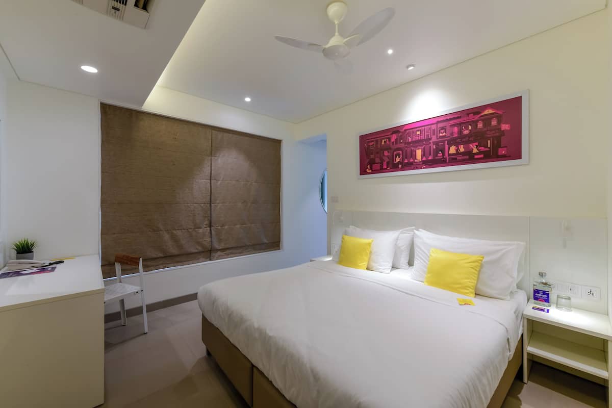 A modern hotel room with a bed, bedside table, and a desk with a chair.