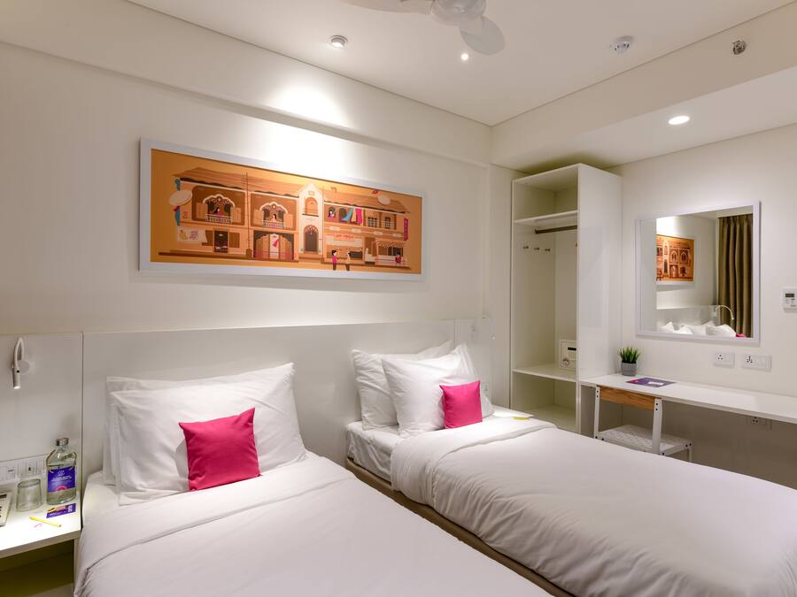Habitación de hotel con dos camas, una mesita de noche con teléfono, un espejo y un cuadro en la pared.