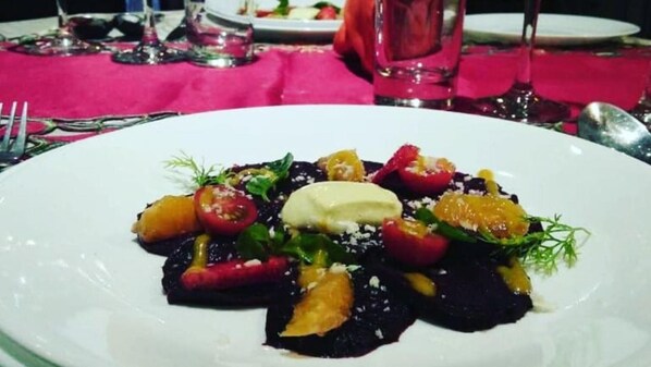 A white plate with a salad consisting of tomatoes, greens, and possibly some fruit, accompanied by a dollop of cream or sauce.