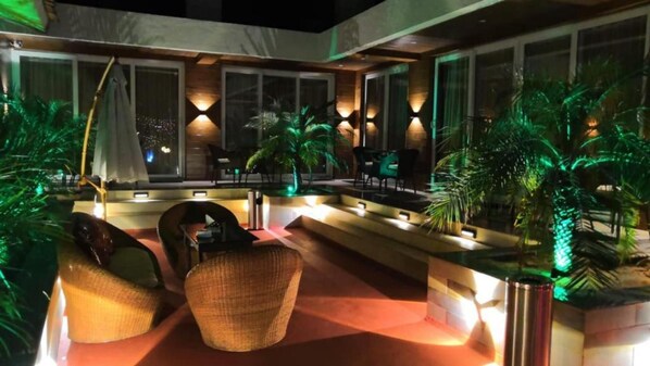 An outdoor lounge area with seating, a pool, and ambient lighting. - Shivers Oasis Luxury rooms (Candolim)