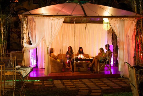 Un área de estar al aire libre con cortinas blancas y una mesa con chimenea.