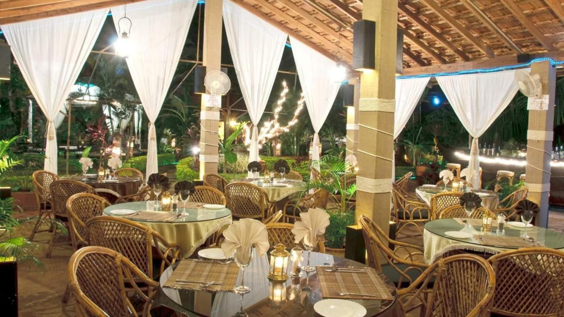 An outdoor dining area with round tables, wicker chairs, and white drapes.