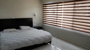 A bedroom with a bed, a nightstand, and a window with blinds.