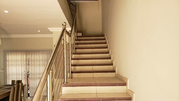 A staircase with beige steps and a metal handrail, leading to a landing.