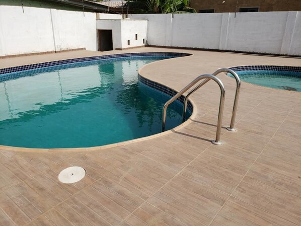 A swimming pool with a curved edge and a metal ladder. - City Enclave Luxury Condo (Accra)