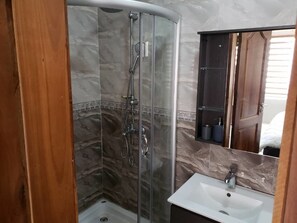 A bathroom with a glass-enclosed shower, a white sink, and a wooden cabinet. - City Enclave Luxury Condo (Accra)