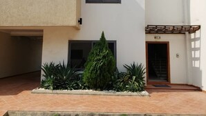 A modern building with a tiled patio, a small garden with various plants, and a staircase leading to an entrance.