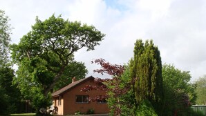 Een laag huis van baksteen met een schuin dak, een voortuin en een oprit naar de ingang.