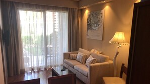 A living room with a sofa, a small table, and a chair. There is a window with curtains, a lamp, and a framed picture on the wall. - Premium apartment on the Beach Oazis Hotel (Kobuleti)