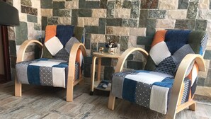 Two armchairs with a patchwork cushion design, placed on a wooden floor with a stone wall in the background. - Premium apartment on the Beach Oazis Hotel (Kobuleti)