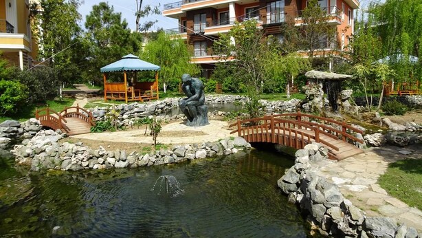 A landscaped garden with a pond, a statue, and a wooden bridge. - Premium apartment on the Beach Oazis Hotel (Kobuleti)