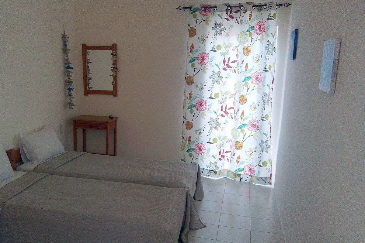 A bedroom with two beds, a wooden nightstand, a mirror, and a floral curtain.