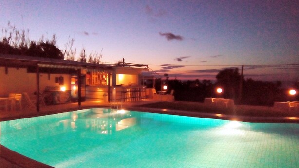 Une piscine à l’eau d’un bleu limpide, entourée d’un bâtiment doté d’un espace extérieur aménagé avec des sièges et un bar.