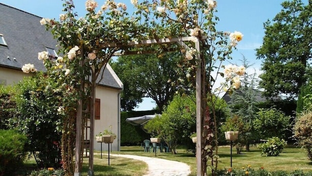 A garden with a pergola covered in flowers, a pathway, and outdoor seating. - Chambres d'hotes de la Ville Patouard (Tremereuc)