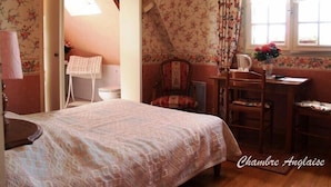 A bedroom with a bed, a desk, and a chair. There is a window with curtains, a lamp, and a vase with flowers. - Chambres d'hotes de la Ville Patouard (Tremereuc)
