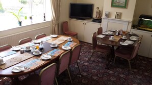 Un coin repas avec deux tables préparées pour le petit-déjeuner, un téléviseur posé sur un meuble et un aquarium accroché au mur.