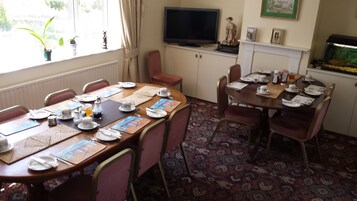 Un comedor con dos mesas dispuestas para el desayuno, un televisor sobre un mueble bajo y un acuario en la pared.