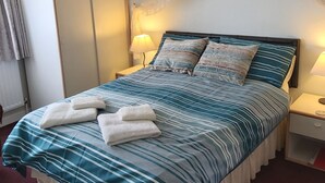 Un lit bien fait, avec une literie à rayures et deux serviettes, une table de chevet avec une lampe et une armoire dans une chambre d’hôtel.