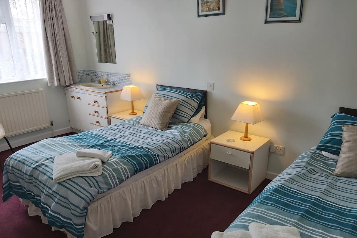 Ett hotellrum med en säng, sängbord, en spegel, ett fönster med gardiner och ett element.