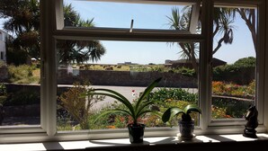 Une fenêtre donnant sur un jardin, une statue et un bâtiment situé au loin.