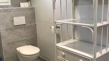 A bathroom with a toilet, a white metal shelf unit with drawers, and a towel rack.